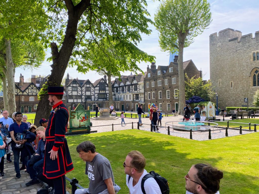 A group of tourists listening to a guided tour of the Tower of London on a beautiful sunny day in London, England.